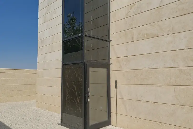 Side view of a modern outdoor glass home lift installed next to a building
