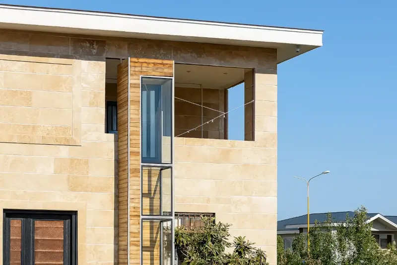 Glass home lift with wooden exterior installed outside a modern villa